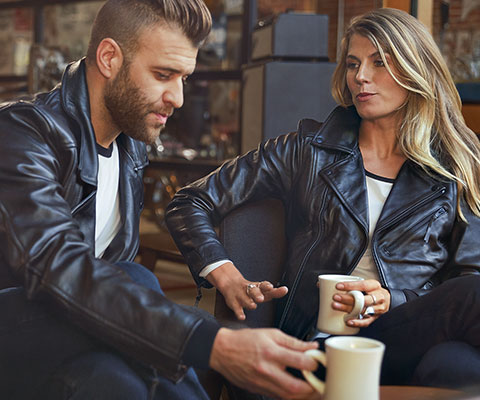 L'immagine mostra un giovane con una giacca in pelle FlatTwin da uomo e una ragazza seduta accanto a lui con una giacca in pelle FlatTwin da donna.
